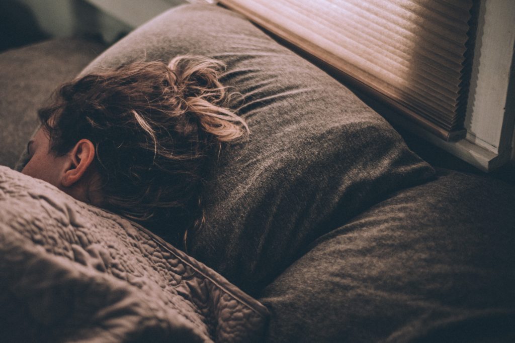 gregory-pappas-rUc9hVE-L-E-unsplash Eine Frau liegt schlafend im Bett, eingekuschelt in ihrer braunen Bettdecke.