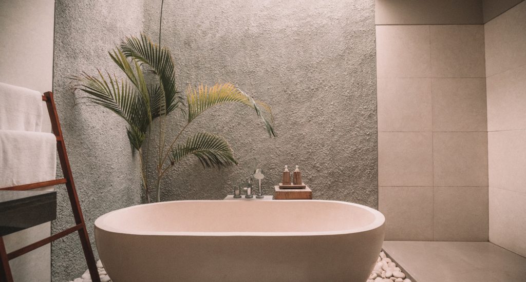 Freistehende Badewanne mit Pflanze vor strukturierter Wand.