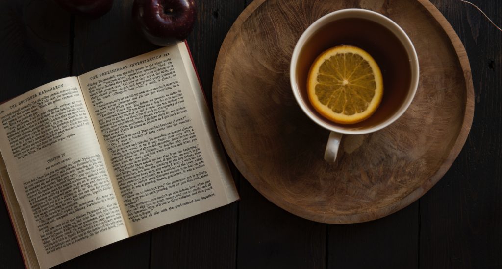 Links liegt ein Buch, rechts steht eine Tasse Tee mit einer Zitronenscheibe im Innern, die das Immunsystem stärken soll.